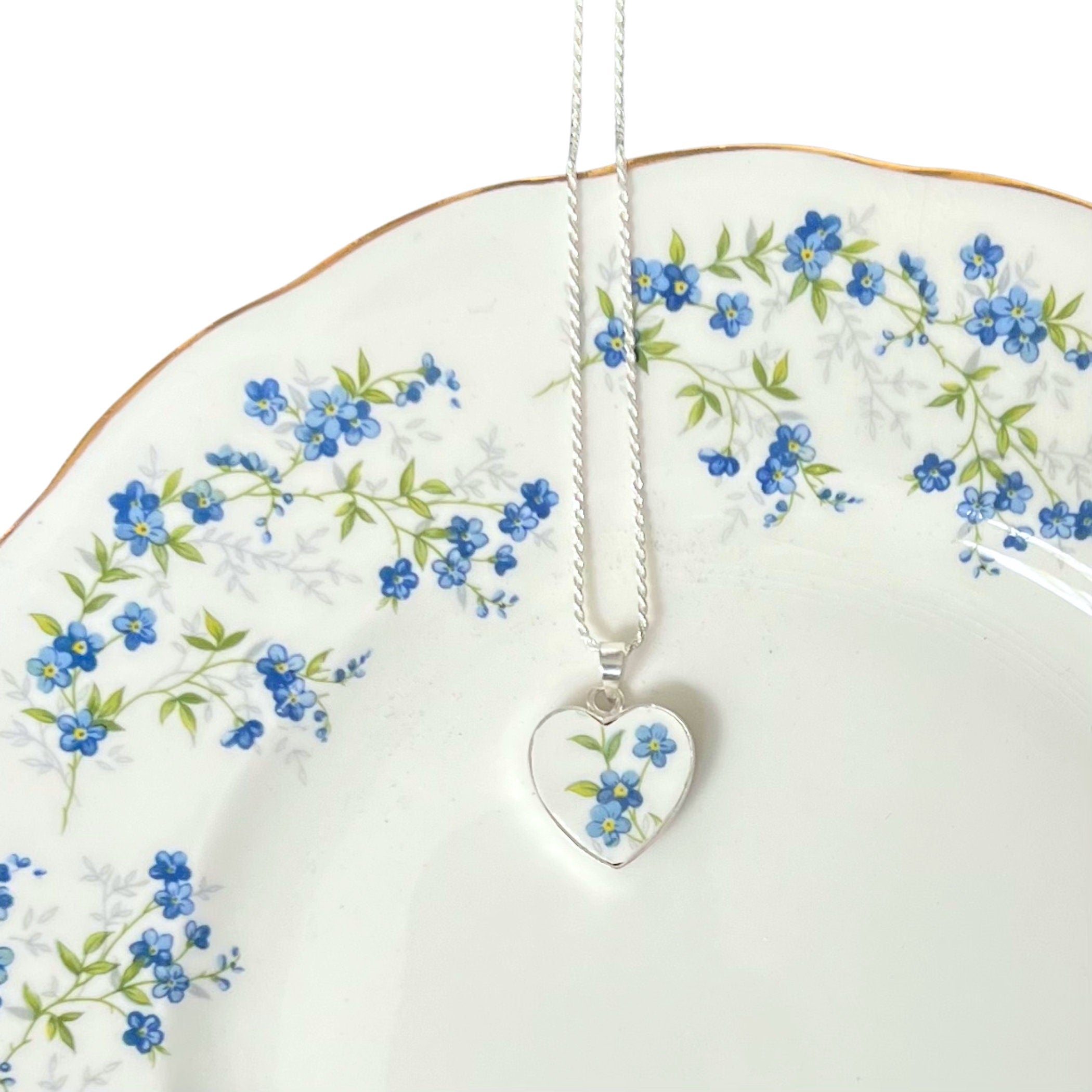 A photo of a handmade forget me not heart necklace, handmade with upcycled vintage Queen Anne china and sterling silver.