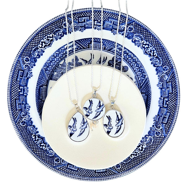 Three Blue Willow Love Birds necklaces — the oval, teardrop, and round pendants with chains — displayed on the vintage china plate they were cut from.