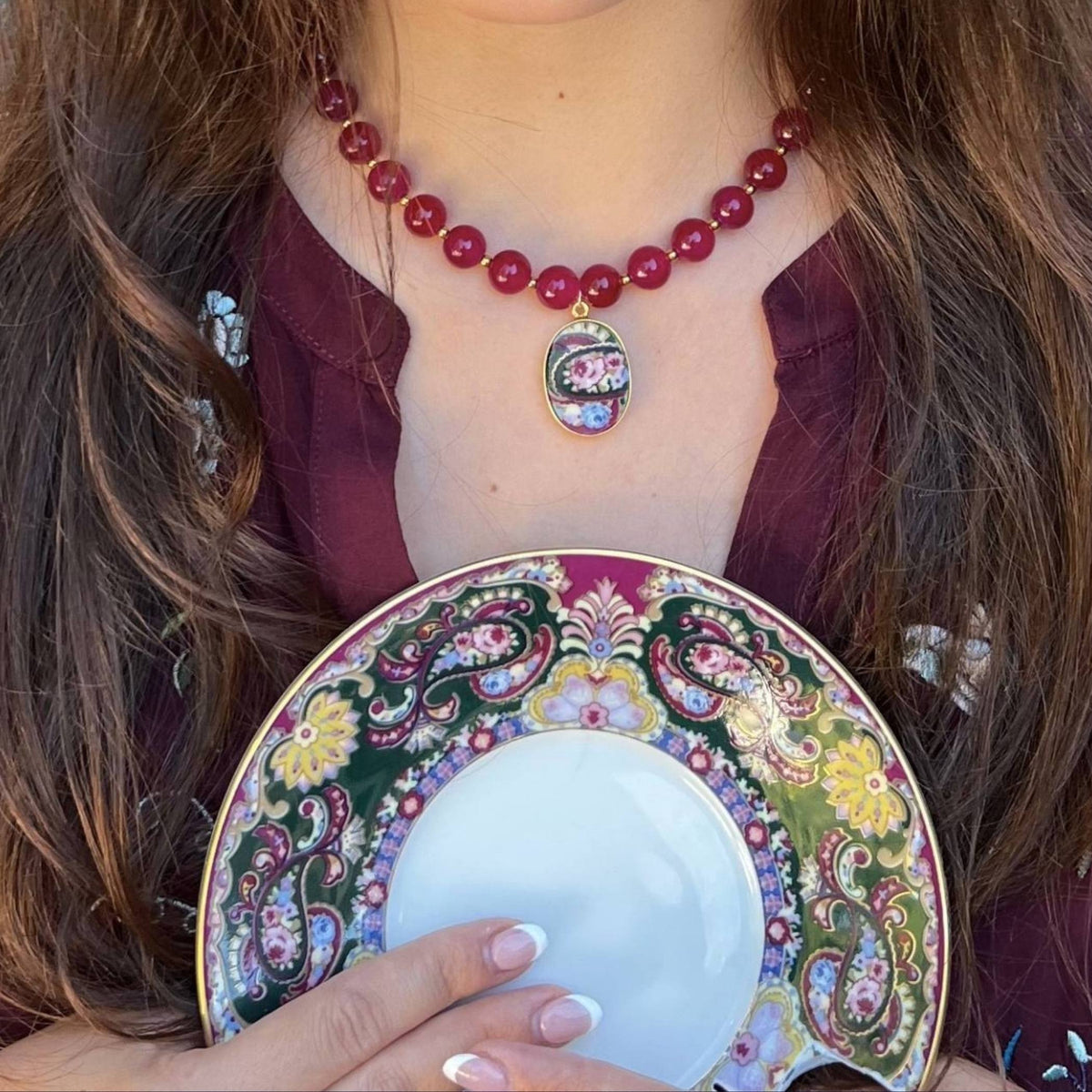 Close-up of the burgundy beaded and rose porcelain pendant necklace worn with an outfit in coordinating jewel tones.