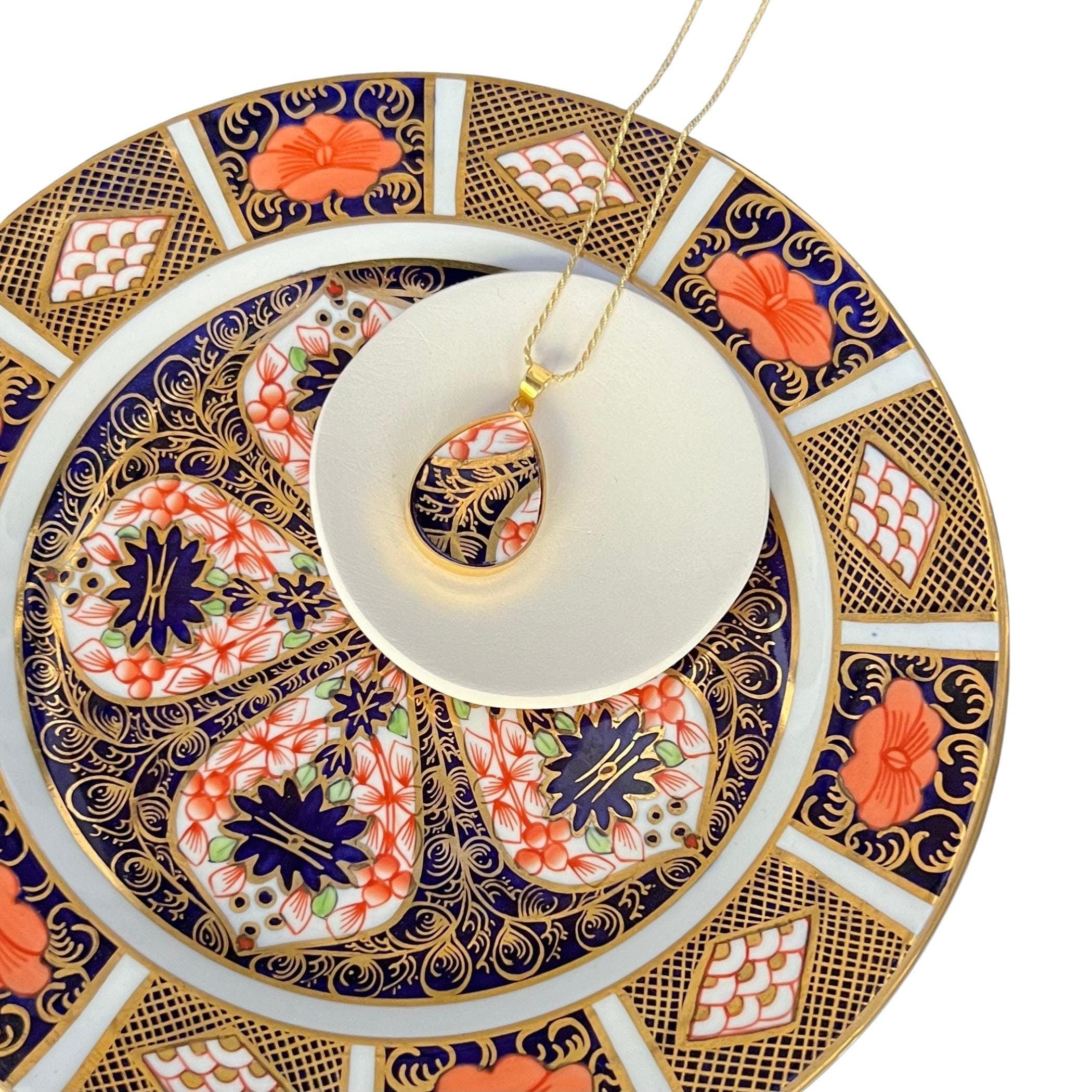 Intricate Royal Crown Derby Old Imari porcelain teardrop pendant necklace displayed on the antique plate it was upcycled from.