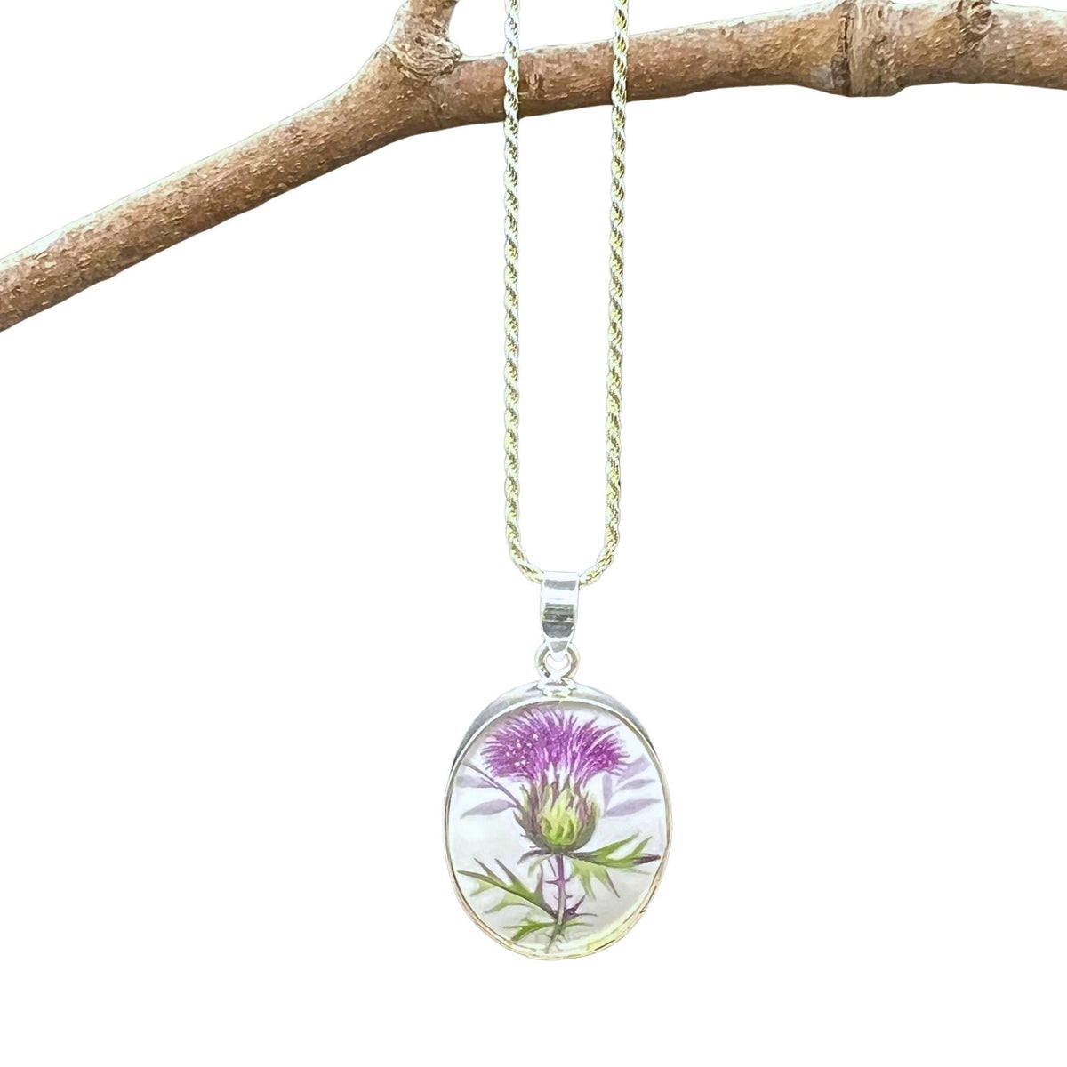 Purple Scottish thistle china necklace hanging on a branch, showing the sterling silver chain.