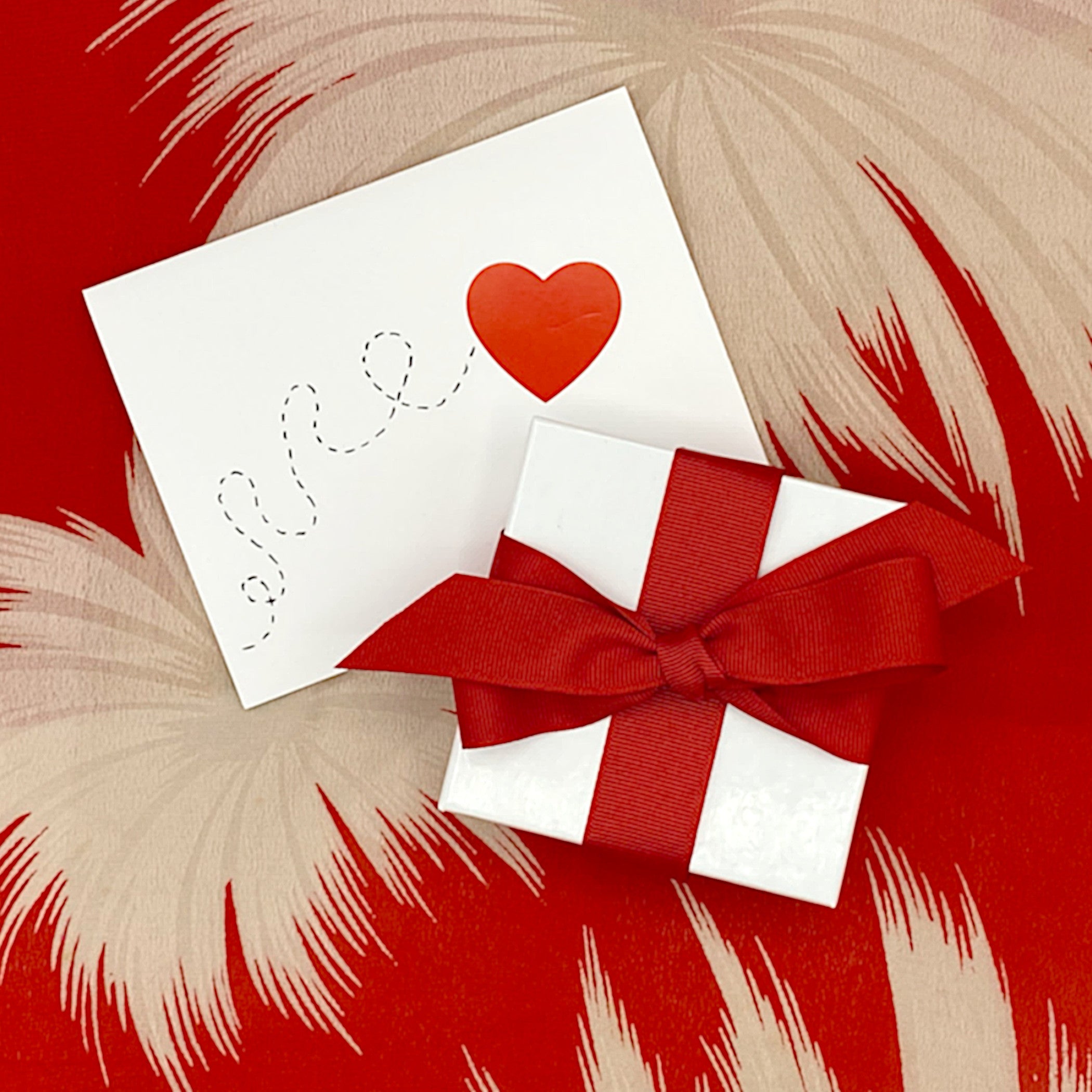 A gift box with a red ribbon and a card with a red heart.