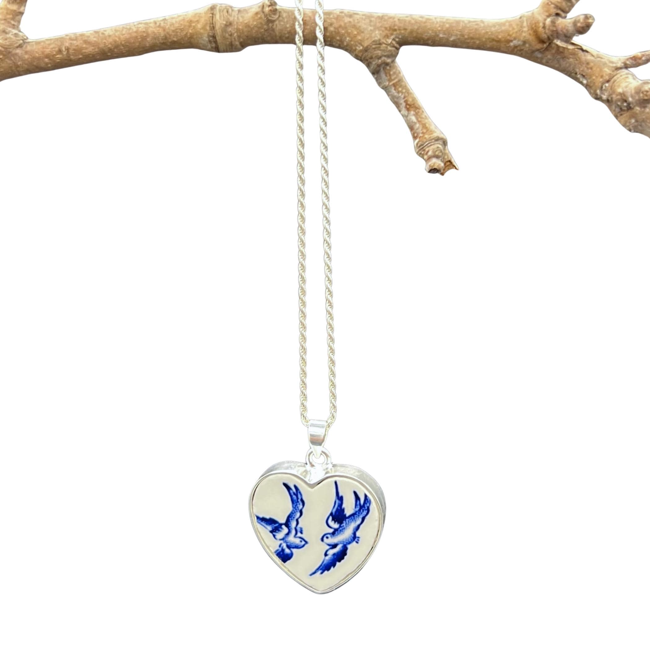 Blue Willow Love Birds heart necklace hanging from a branch, showing the heart pendant and sterling silver chain.