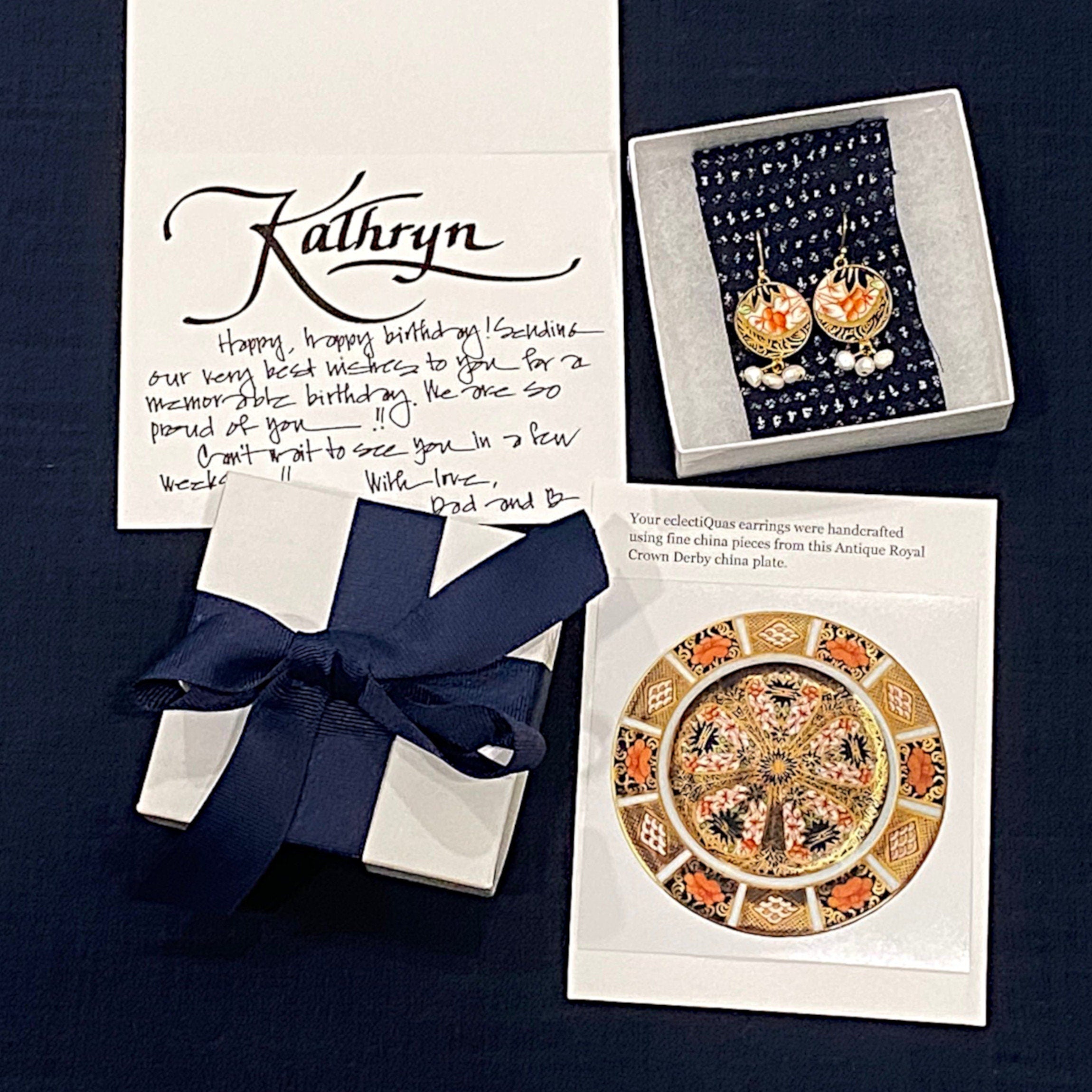 eclectiQuas signature packaging: a white box with an indigo ribbon, a decorative fabric strip inside each box corresponding to the design and color of each jewelry item, and a photo card showing the plate from which the broken china pieces originate.