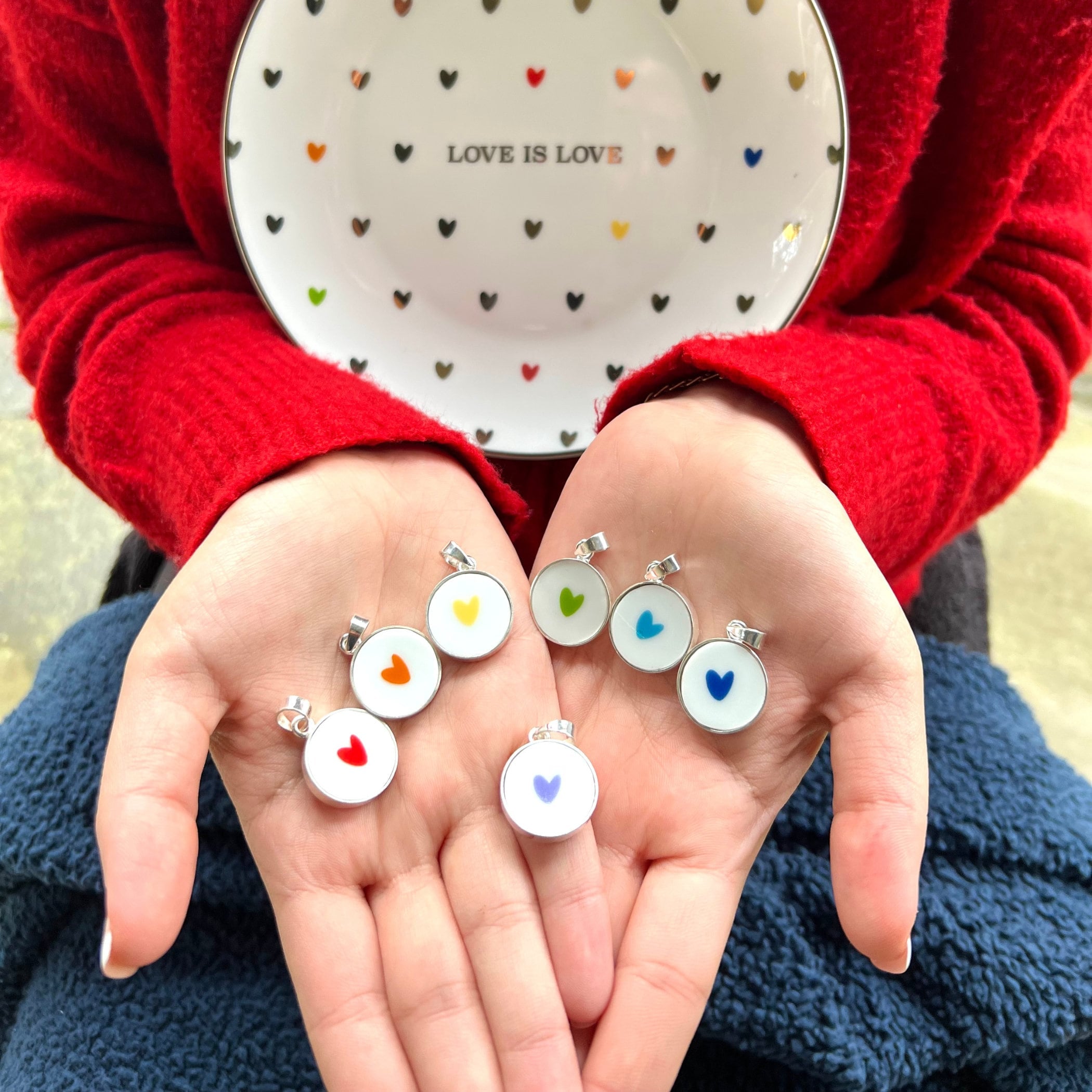 May include: A set of six silver pendants with colorful heart designs. Each pendant features a white background with a single heart in a different color: red, orange, yellow, green, blue, and purple.