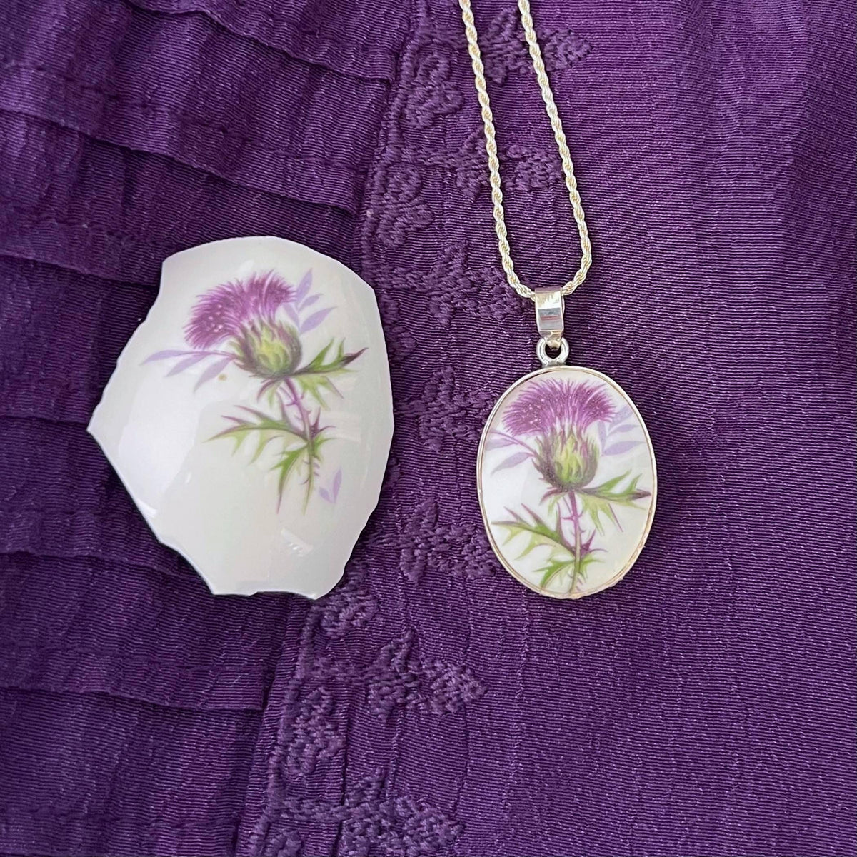 Purple Scottish thistle necklace displayed next to a broken china piece from the same vintage china salt shaker it was upcycled from.