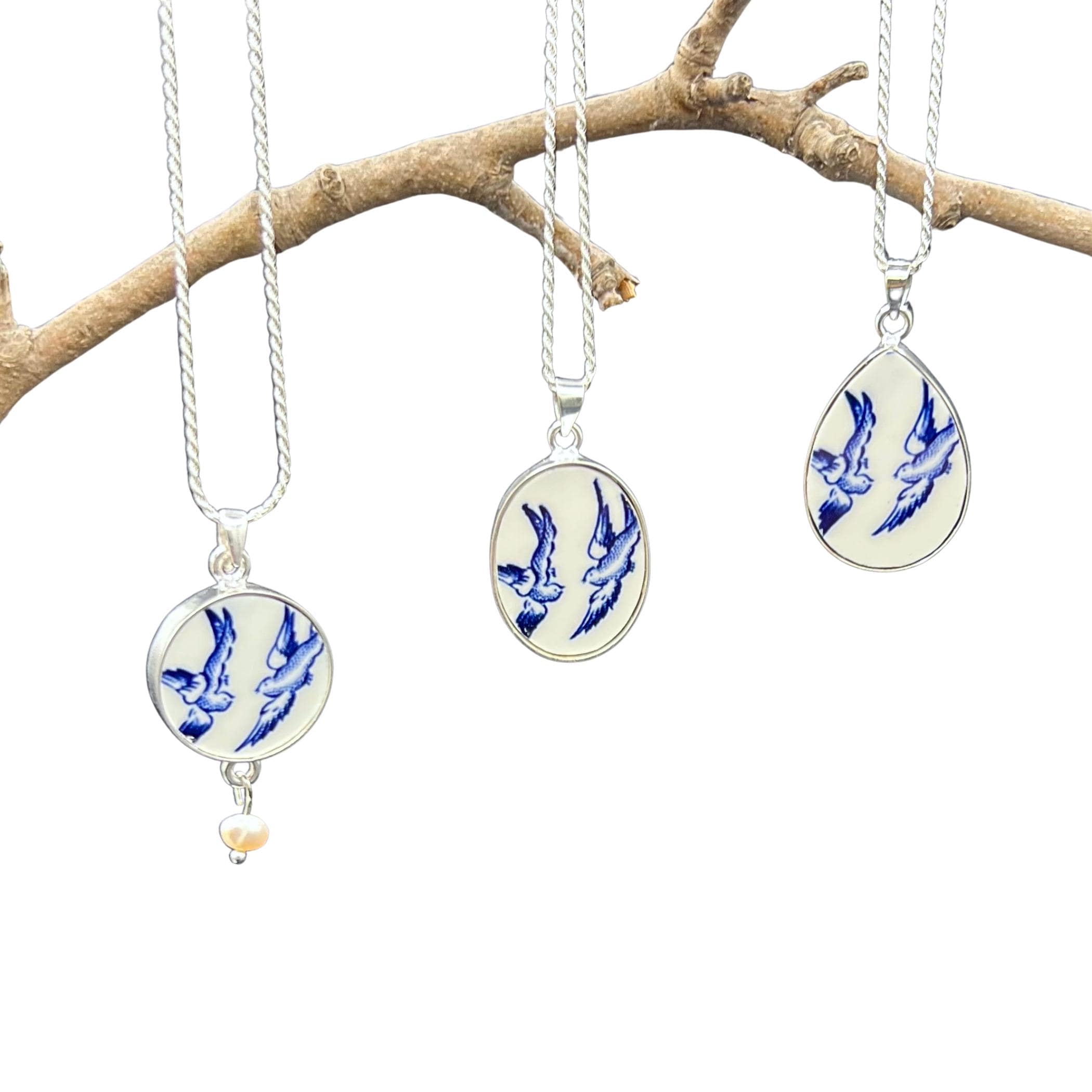 The three Blue Willow Love Birds necklace  pendants hanging from a branch, showing the round, oval and teardrop pendant shapes and the sterling silver chains.
